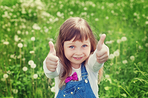child in field giving thumbs up
