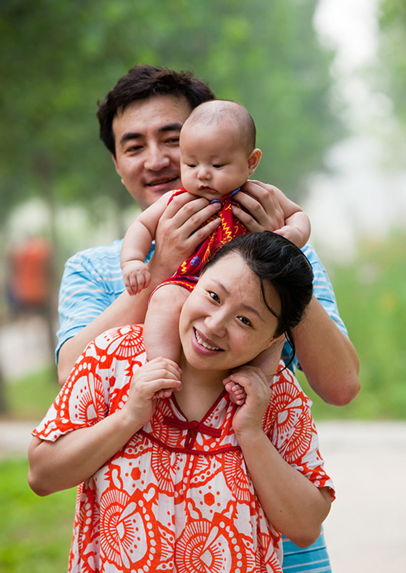 asian family of three at the park. baby on shoulders of mom